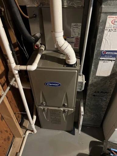 Carrier heating unit in a basement installation with piping and air flow label.