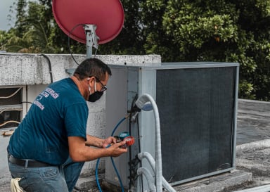 Technician servicing an air conditioning unit on a rooftop.
