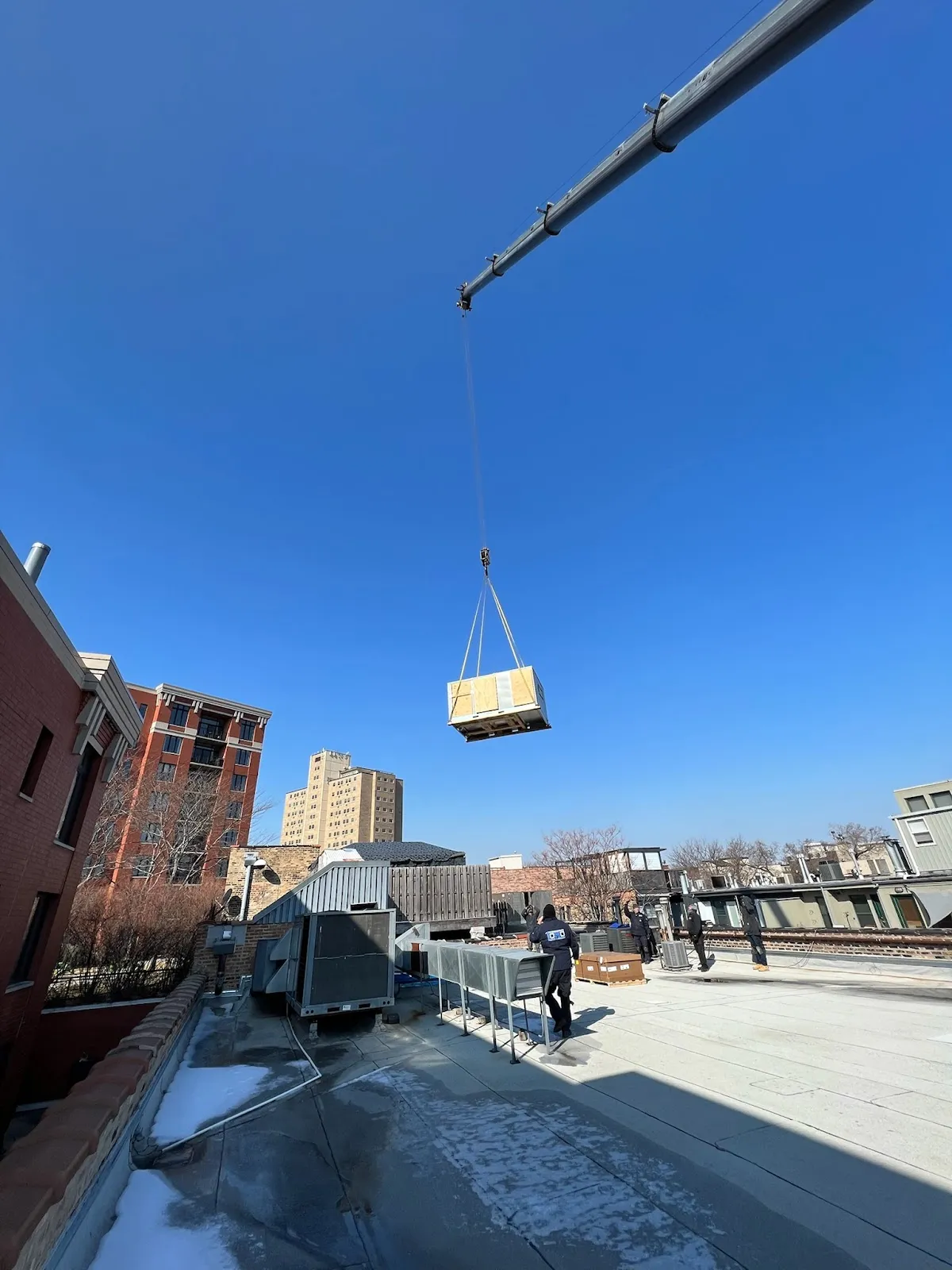 A crane lifting a large wooden crate against a blue sky.